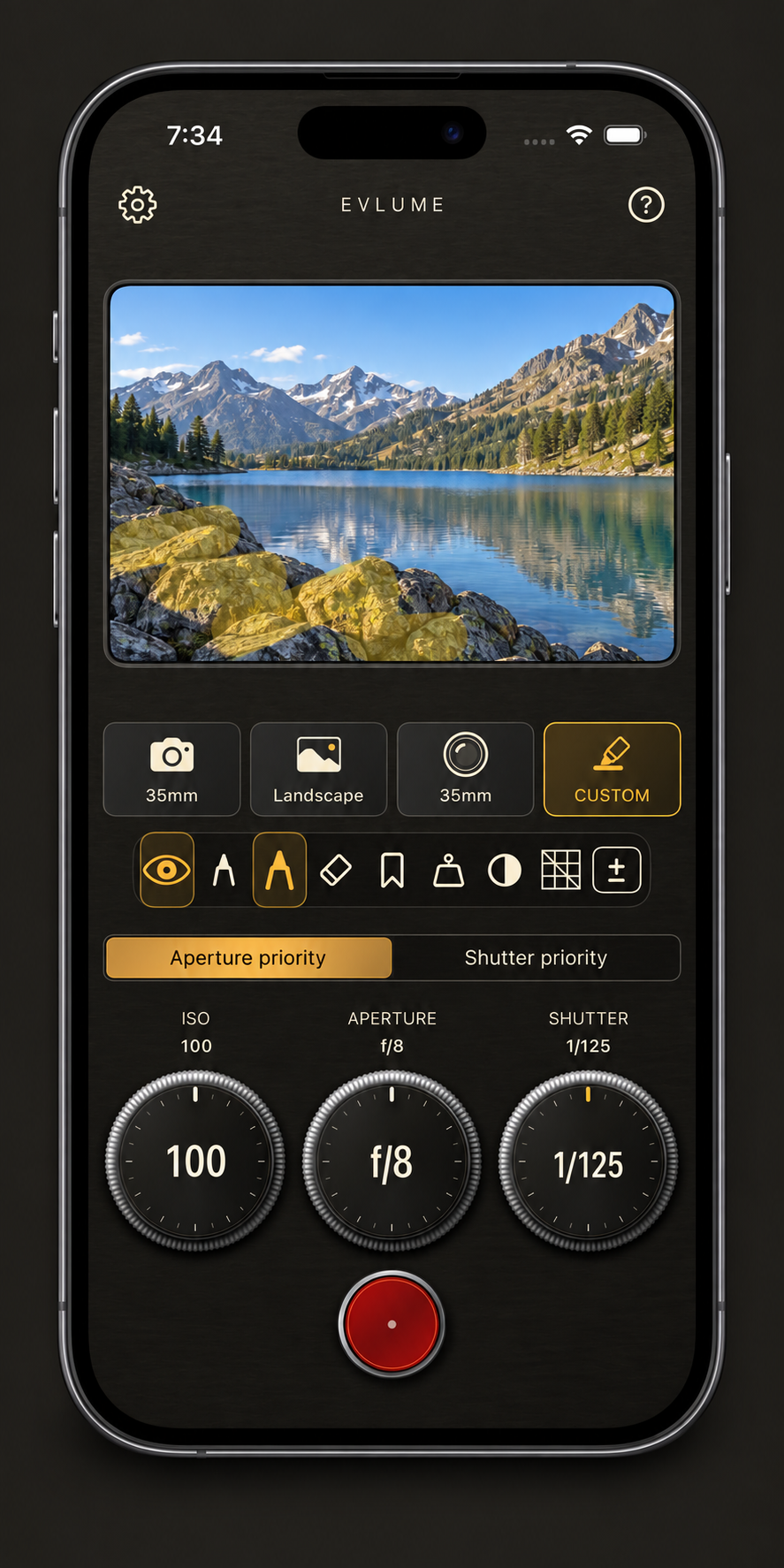 An iPhone displaying an illustrative Evlume Custom metering preview of a mountain lake with foreground rocks highlighted in yellow.